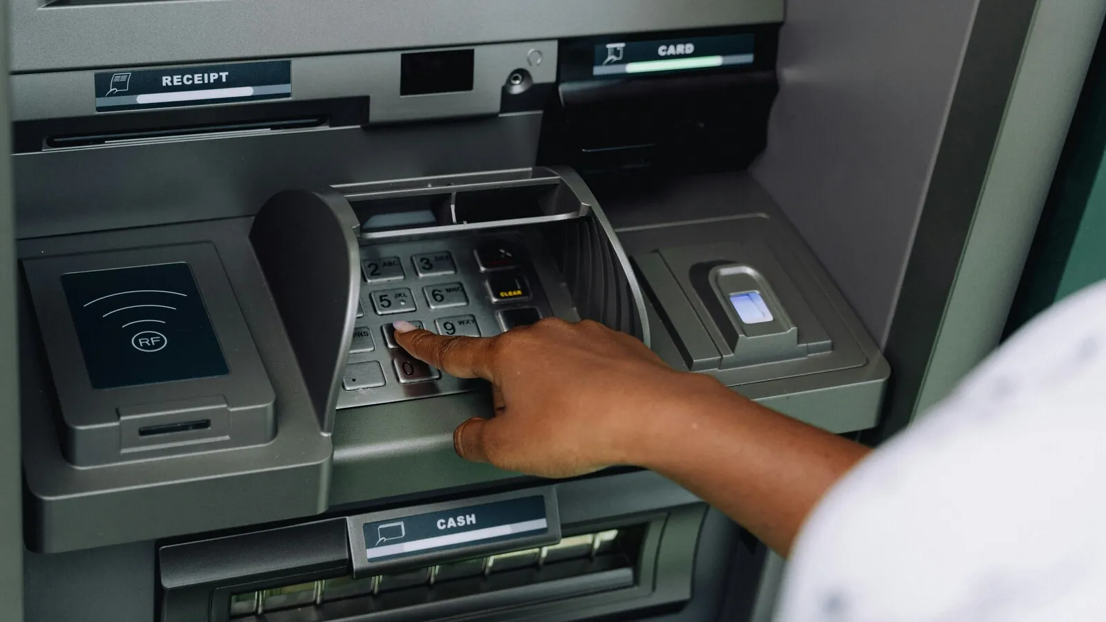 Close-up of a hand using an ATM keypad, with contactless reader and fingerprint scanner visible
