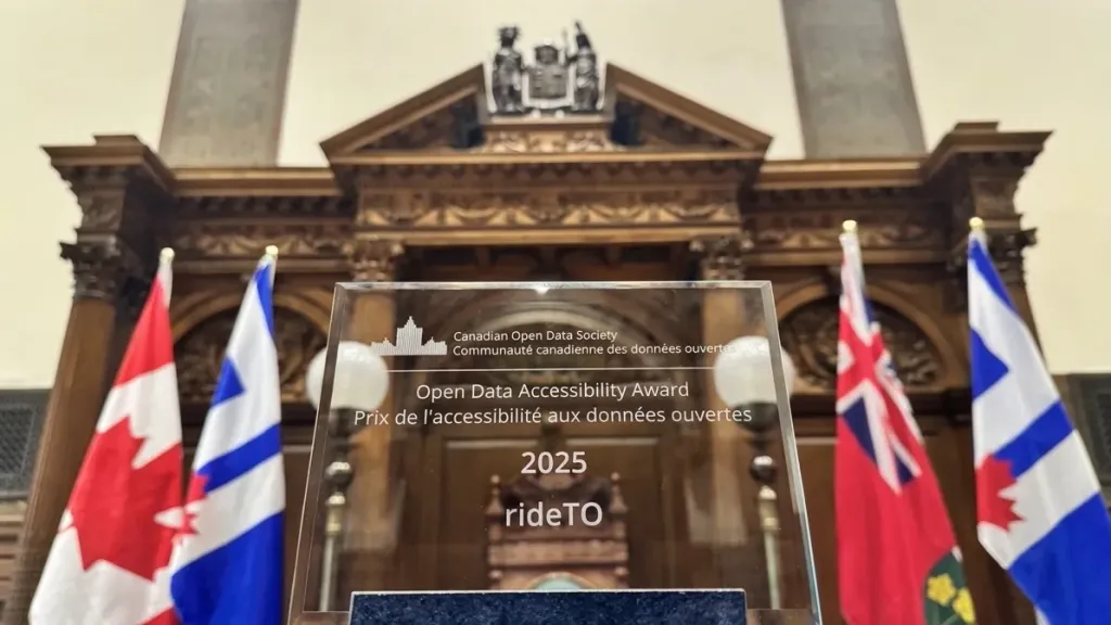 The Open Data for Accessibility Award 2025 by Canadian Open Data Society for rideTO, set against ornate wooden architecture and surrounded by flags